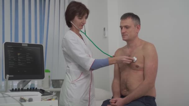 Il medico curante caucasico utilizza il fonendoscopio per esaminare la frequenza cardiaca del paziente maschile alla consultazione in ospedale. — Video Stock