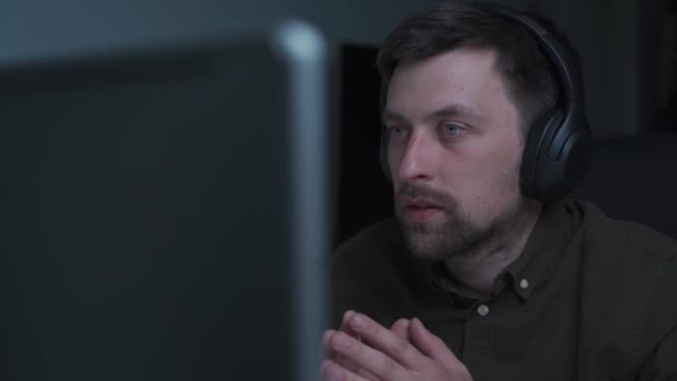 Evden uzakta çalışan serbest çalışan genç bir adam. Kulaklıklı bir erkek bilgisayardaki bilgisayarda görüntülü konuşma yapıyor. Öğrenci ve e-öğrenme süreci konsepti. Çevrimiçi konferans konuşması — Stok video