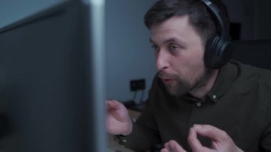 Rahatsız, öfkeli, kulaklık takan genç bir erkek bilgisayarda video görüşmesi ya da konferans görüşmesi yapıyor, tartışıyor, küfrediyor ve iş arkadaşlarına ve meslektaşlarına bağırıyor. Kötü habere tepki.