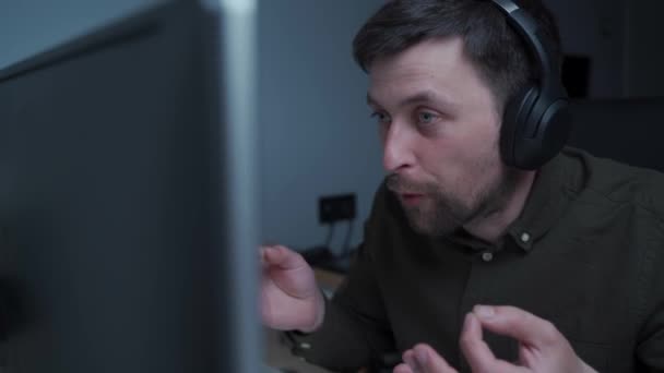 Znepokojený, rozzlobený dospělý muž ve sluchátkách, který má na počítači videohovor nebo on-line konferenční hovor, hádá se, nadává a řve na kolegy a kolegy. Reakce na špatné zprávy. — Stock video