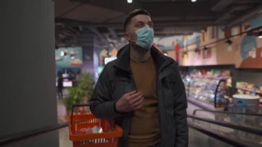 Maske yok, giriş yok. Yeni kural. Marketteki yürüyen merdivende elinde alışveriş sepeti olan biri karantina yönetmeliği sırasında koruyucu maske takıyor. Coronavirüs, Coperid 19. Tüketim ve insanlar