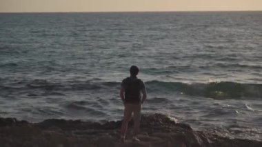 Sırt çantalı bir turist gün batımında Akdeniz 'de duruyor. Sırt çantalı bir erkek gezgin doğayı keşfediyor. Seyahat tutkusu