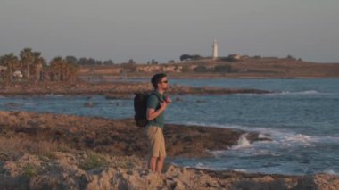 Sırt çantalı bir turist gün batımında Akdeniz 'de duruyor. Sırt çantalı bir erkek gezgin doğayı keşfediyor. Seyahat tutkusu