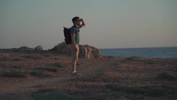 Cyprus reisthema. Een reiziger met een rugzak kijkt naar de zonsondergang op de Middellandse Zee op een rotsachtige kust in de buurt van de stad Paphos — Stockvideo