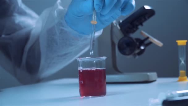 Close-up da mão de um trabalhador de laboratório médico em um terno de proteção e luvas tira amostras de líquido vermelho com uma pipeta — Vídeo de Stock