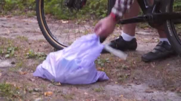 Atleta in bicicletta attraverso la foresta con sacco della spazzatura sul manubrio, pulizia spazzatura e plastica durante un viaggio in bicicletta nella foresta. Tema ecologia, inquinamento, rifiuti e plastica scartati — Video Stock