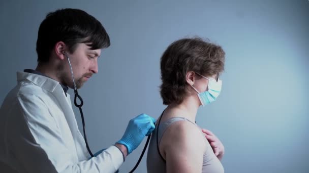 Médico pneumologista masculino faz um exame médico de uma paciente com um coronavírus e tem problemas com os pulmões e respiração pesada e tosse em um fundo cinza no hospital — Vídeo de Stock