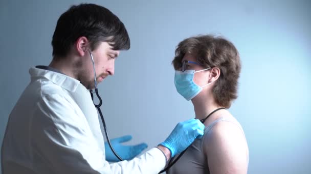 Врач-мужчина проверяет дыхание пациентки в медицинской маске на сером фоне. — стоковое видео