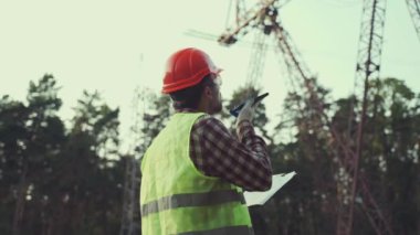 Güç sistemleri mühendisi geldi. Bir mühendis cep telefonuyla konuşuyor ve verileri bir elektrik hattı ağıyla karşılaştırıyor.