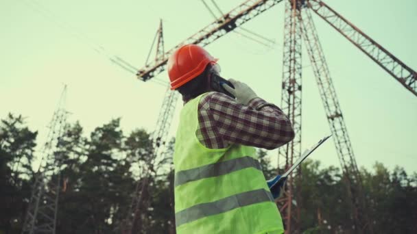 Un ingeniero eléctrico está trabajando. Habla por teléfono. Comprobando la red eléctrica. Energía. Industria — Vídeos de Stock