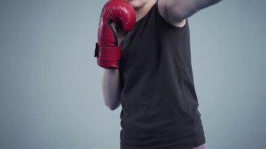 Spor salonunda arka planda gri bir duvarın arkasında kırmızı boks eldivenleriyle poz veren genç ve güzel bir kadın. Sahne arkasında, video çekiminde.
