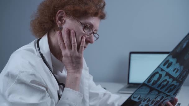 Odaklanmış kadın doktor bir hastanın akciğerlerinin röntgenlerini inceliyor. Hastanede çalışan kıdemli pratisyen. — Stok video