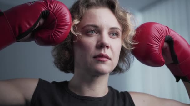 Le thème des femmes dans les arts martiaux. légitime défense pour la femelle. boxer féminin en gants rouges posant sur un fond gris lors d'une séance photo, en coulisses vidéo — Video