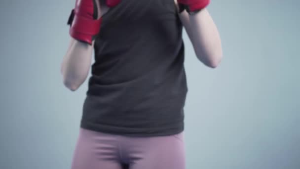 Temat kvinnor i kampsport. Självförsvar för kvinnan. Kvinna boxare i röda handskar poserar på en grå bakgrund under en fotografering, backstage video — Stockvideo