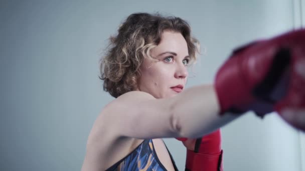 Mladá krásná štíhlá žena pózující v červených boxerských rukavicích v tělocvičně na pozadí šedé stěny během focení, zákulisí videa — Stock video