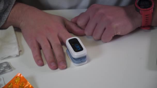Молодой кавказский мужчина использует монитор насыщения крови кислородом для определения уровня SpO2 в крови во время коронавирусной эпидемии дома, получив плохой результат, стресс и вызывает врача 911. Ковид 19 — стоковое видео