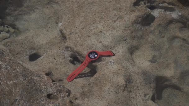 20 de mayo de 2021 Chipre, pathos. Turismo deportes reloj Garmin INSTINCT Llama roja en el agua sobre piedra. El hombre toma vigilancia protegida con la navegación GPS desde el agua de mar transparente para viajar y explorar — Vídeos de Stock