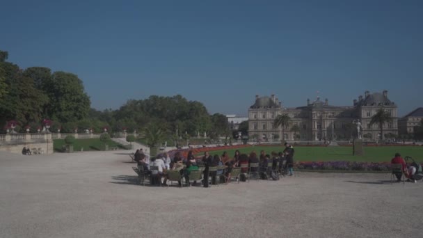 Студенти під час навчання на відкритому повітрі сидять на стільцях по колу і слухають вчителя в Люксембурзьких садах у Парижі 4 вересня 2021 року. Le Jardin du Luxembourg). Громадські сади та Сенат Франції — стокове відео