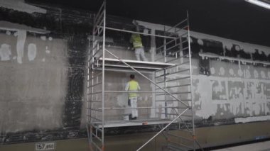 20 Nisan 2022, Münih. Almanya. İnşaatçılar Münih 'teki bir metro istasyonunu tamir ediyorlar, eski duvarı onarmak için sıva aleti kullanıyorlar. Metro işçisi tüp durağını tamir ediyor. Duvar macun bıçağıyla sıvanmış.