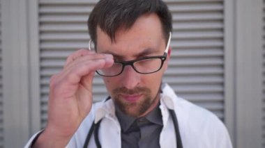 Salgın koronavirüs ve kovid 19. Ciddi genç Kafkasyalı doktor klinikteki hastaları görmek için dönmeden önce maske takıyor. Doktorların üzüntüsü, büyük ameliyatların ardından stres ve yorgunluk yaratır..