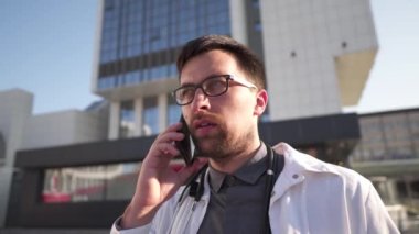 Beyaz önlüklü genç Kafkasyalı doktor hastane molasında cep telefonuyla hastaya danışıyor. Klinik yakınlarında cep telefonuyla konuşan bir tıp çalışanı. Üniformalı doktor telefonda konuşuyor..
