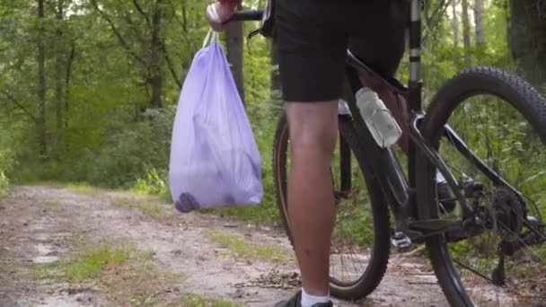 森の中を自転車に乗ってゴミを集める 環境を保護するためのトレンディスポーツプログラムのプラグ 汚染だ 生態学的問題 組み合わせスポーツとエコクリーニングの性質 — ストック動画
