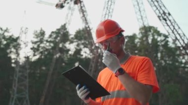 Yüksek voltajlı güç transformatöründeki elektrik mühendisi telsizle ilgili bir sorun bildirdi ve panoya baktı. Yüksek voltaj kulesinin yanında taşınabilir radyosu olan profesyonel elektrikçi. 