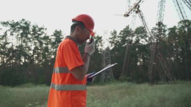 Yüksek voltajlı güç transformatöründeki elektrik mühendisi telsizle ilgili bir sorun bildirdi ve panoya baktı. Yüksek voltaj kulesinin yanında taşınabilir radyosu olan profesyonel elektrikçi. 