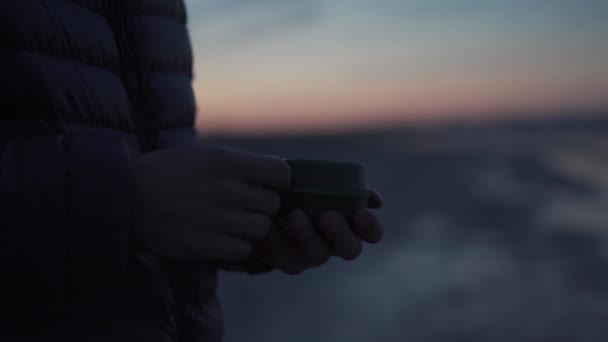 男性游客手牵着游客杯 日落时喝一杯热饮的特写镜头 在露营时 可倾覆的野营杯和茶在一个旅行者的膨胀 冬天的早晨 湖面上 旅行生活方式 — 图库视频影像