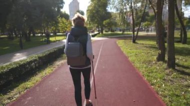 İskandinav teması yaşlılıkta sırıklarla yürümektir. Aktif eğlence ve yaşlılıkta egzersiz. Yürüyüş sopalı bir kadın güneşli bir havada parkta koşu pistinde yürüyor. İskandinav çubukları