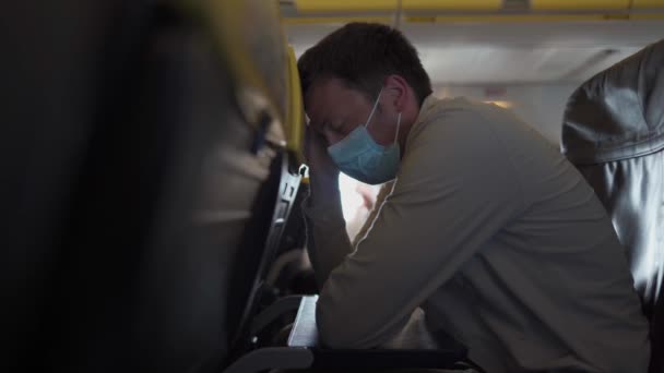 防護マスクをしたハンサムな男は隔離された日に飛行機の座席で寝ることを試みる 飛行中に飛行機の中で寝ている顔のマスクの白人男性 Covid 19パンデミックの概念の後の新しい正常な旅行 — ストック動画