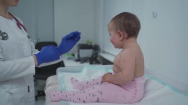 Pediyatrist doktor konsepti. Çocuklar için tıbbi bakım. Bir yaşındaki kız bebek klinikteki kadın çocuk doktoru tarafından muayene edildi. Sağlık kontrolü için çocuk doktoru ziyaret ediyor. Doktor küçük hastayı muayene ediyor..