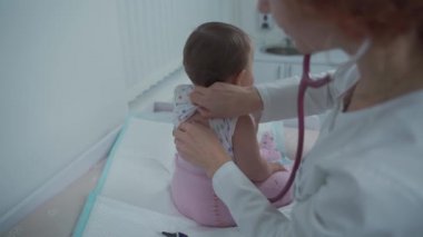 Pediyatrist doktor konsepti. Çocuklar için tıbbi bakım. Bir yaşındaki kız bebek klinikteki kadın çocuk doktoru tarafından muayene edildi. Sağlık kontrolü için çocuk doktoru ziyaret ediyor. Doktor küçük hastayı muayene ediyor..