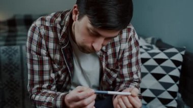 Endişeli adam hamilelik testine evde bakıyor. Kocası hamilelik testi sonuçlarına üzülmüş. Erkek, karısı negatif hamilelik testi yüzünden üzgün. Bir daha babam gibi olmayacağım. Baba olmak için çok gencim.