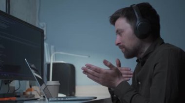 Teknoloji ve akıllı çalışma konsepti. Kulaklık takan bir bilişim programcısı bilgisayar üzerinde çalışan meslektaşlarıyla konuşuyor. Erkek web sitesi geliştiricisi, yazılım mühendisi bir uygulama geliştiriyor, video oyunu. 