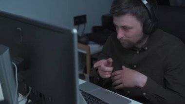 Kulaklık takmış beyaz bir adam ev ofisinden bilgisayarlı ekran görüntülerine bakıyor. Kulaklık takan genç bir erkek web sitesinde ders alıyor ya da internette eğitim görüyor. Uzaktan eğitim kavramı, video çağrısı.