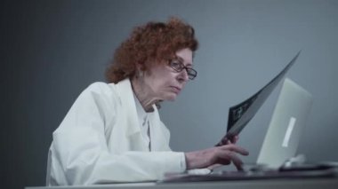A senior woman doctor is doing the patients chest CT scan on a laptop in the office. A mature female radiologist types up a description of a pulmonology MRI scan on a laptop. Diagnostic radiology.