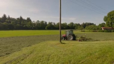 A farmer in Bavaria cuts the grass in a field in summer. Farmer with agricultural equipment mows the meadow and makes hay. Hilly foothills of the Alps, blue sky, Bavaria