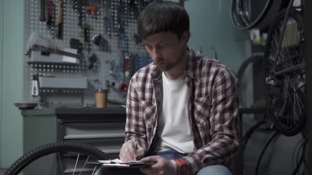 Male Bicycle Mechanic Calculates Cost Repairing Cycle Pen Clipboard Hand — Αρχείο Βίντεο