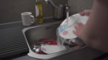 Temizlikçi kadın mutfakta bulaşık yıkıyor. Bulaşık yıkayan kadın elleri. Temizlik sabunu, bulaşık yıkayan biri. Kadın elleri mutfak lavabosunda bulaşık yıkıyor. Ev kavramı