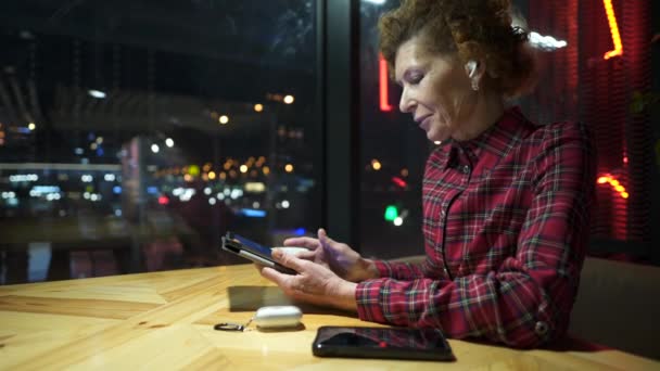 Senior Woman Wearing Headphones Video Conferencing Tablet Cafe Sitting Window — 图库视频影像