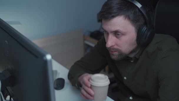 Tired Man Works His Computer Drinks Coffee Uses Headphones Programmer — Stok video