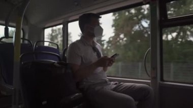 Man sits on bus wearing protective mask ffp2 uses smartphone in Germany, Munich. Passenger in protective mask in public transport and surfing Internet. Coronovirus rules of personal protection 