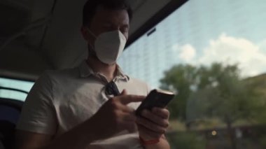 Commuting during pandemic. Public transportation curfew. Using cell phone while commuting to work on public transportation bus while wearing mask to prevent corona virus. Social distancing on bus 