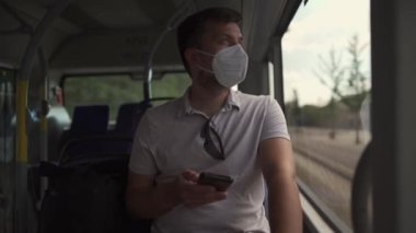 Commuting during pandemic. Public transportation curfew. Using cell phone while commuting to work on public transportation bus while wearing mask to prevent corona virus. Social distancing on bus 
