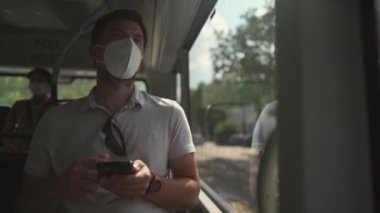 Commuting during pandemic. Public transportation curfew. Using cell phone while commuting to work on public transportation bus while wearing mask to prevent corona virus. Social distancing on bus 