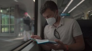 Passenger on public transport reading book while sitting by the window in protective mask. Man traveling on Deutsche Railroad train wearing protective mask and enjoying book. German National Railway. 