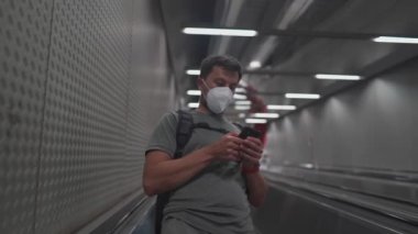 A commuter walks down the subway stairs in a ffp2 mask and uses his phone. Masked man browsing the Internet on a smartphone on an elevator in the metro. Tube in Munich. U Bahn. Deutschland metro