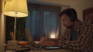 Student communicates online with teacher, uses headphones and laptop at home, writes notes, prepares for university test, college examination, watches educational webinar. Online education concept. 