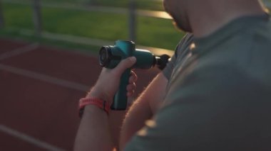Athlete massages with percussion therapy gun to relieve pain of muscle aches after workout. Man massages his body with massage percussion device after training session. Muscle warming up with massager